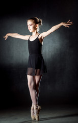 Ballerina. Cute little girl posing and dancing in studio. A little dancer. Dark background. Black dress.