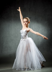Fototapeta premium Young girl ballerina showing the dance elements on a dark background. Ballet. A little dancer.