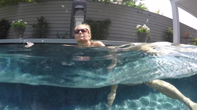 Camera half above and half below water, a beautiful, slim, caucasian woman wearing string bikini swims from right to left. Camera follows her.