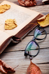 Eyeglasses near open book with autumn leaveson wooden table.Autumn mood concept.