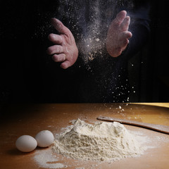 Female hands clapping and sprinkling flour over a wooden kitchen worktop, preparation for baking,...