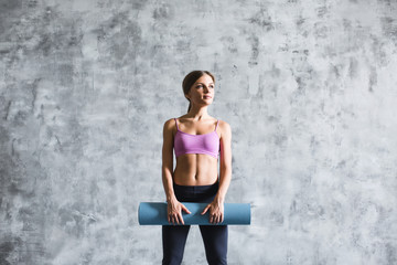 Woman ready for workout standing holding yoga mat.