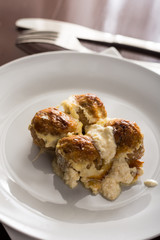 Baked meatballs with cheese served on a white plate with fork and knife in the background