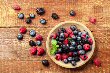 Ripe and sweet berries in bowl on wooden background