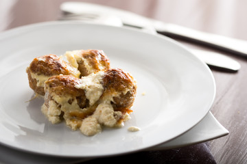 Baked meatballs with cheese served on the white plate with knife and fork
