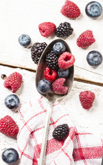 Ripe and sweet berries on vintage metal spoon on wooden white background