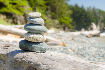 Fototapeta na wymiar Stack of Balanced Stones on Driftwood on a Beach on a Sunny Spring Day. Concept of Meditation and Harmony.