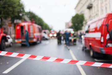 Red and White Lines of barrier tape on the background of firefighters and fire trucks at work.. Red...