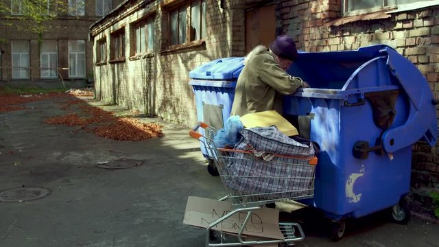 Homeless man searching for empty bottles and other stuff for recycle. Tramp trying to earn money by bringing emty bottles to recycle point.