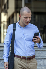 Young handsome businessman standing in front of the building and holding a mobile phone