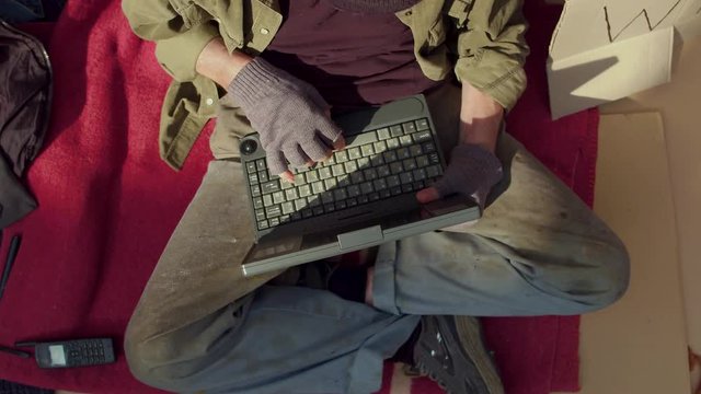 Top view of homeless man playing on laptop. Tramp living in streets using modern technologies.