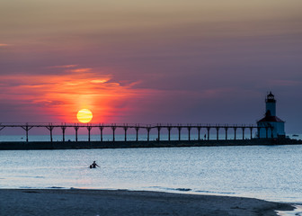 silhouette of a person at the beach in the water with lighthouse in background