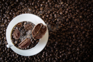 White cup coffee beans with falling beans from top with beans coffee textured background.