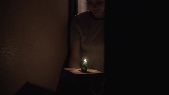 Slow motion shot of mother and son walking in darkness and carrying birthday cake with lit six year old candle