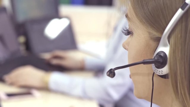 The operator of the hotline with headsets, sit at the computer in the office and advise clients. Workers call-center, a woman talking to customers. She prints on the computer and answers questions.