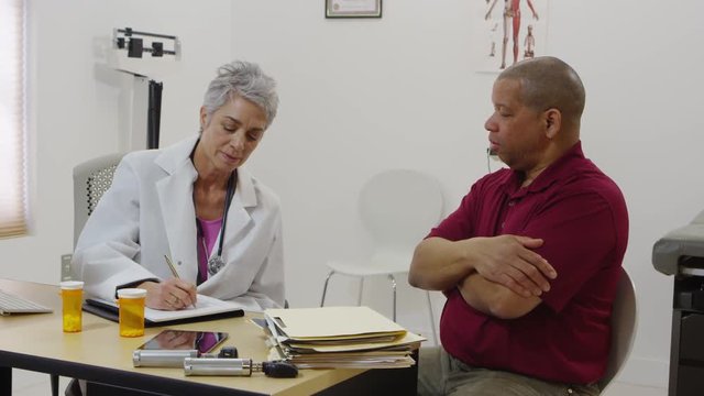 Doctor writing notes and talking with patient in medical office