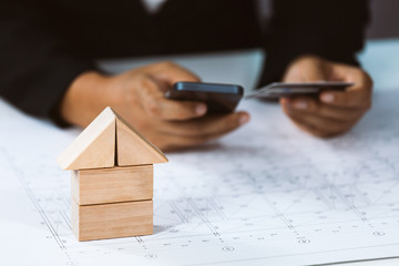 Close-up of house architectural model with businessperson holding credit card and using mobile above project house draw plan