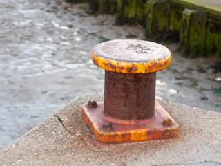 close up of circular top yellow rusted marina metal stump for rope