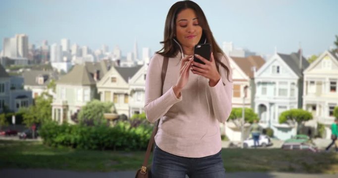 Attractive Hispanic woman listening to music on cell phone and dancing in San Francisco park with view of skyline. Cheerful Latina female dancing to music outdoors in painted ladies neighborhood. 4k 