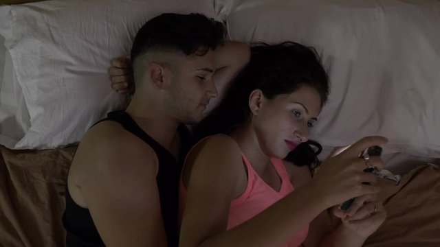Relationship problems with man comforting his wife in bed addicted to her smartphone on social media