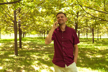 Obraz premium Man with mobile phone in summer park. Young handsome man with smartphone on a sunny day