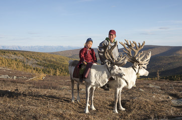 tsaatan man and his son, dressed in a traditional deels, riding reindeers
