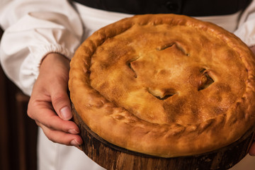 Pie from potato meat cheese and vegetables. Freshly baked pie in hands of woman in uniform