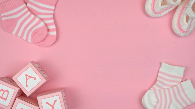 4k Baby girl nursery clothing and accessories overhead on pink wood table, flat lay with copy space, time lapse.