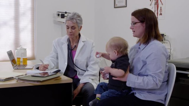 Female doctor talking to mother about baby patient and taking notes