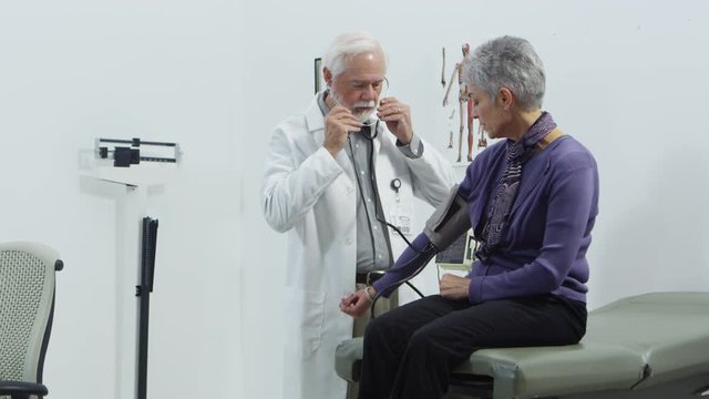 Elderly doctor checking blood pressue of elderly patient