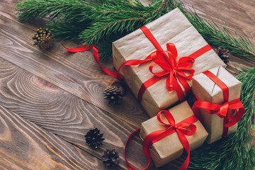 Gifts in festive boxes and green spruce branches on wooden background.