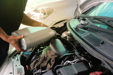 The car mechanic is filling up the engine oil to the customers' car in his car repair shop. Change engine oil in garage shop.