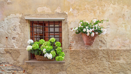 Fototapeta na wymiar An open window with a lattice and flowers on the windowsill. A clay pot with flowers on the wall of the house. Elegantly decorated wall of an old Italian house. Copyspace.
