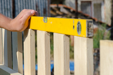 Man building a wooden fence and checking with spirit level. Close up of his hand and tool.