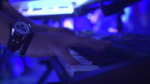 One piano player perform instrumental jazz in bar close up. Professional man play in hall at electronic piano melody of famous songs under flashes of colourful lights. Isolated fingers in movement