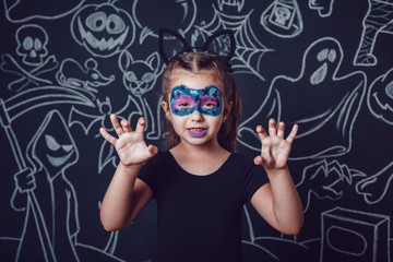 Girl in a cat costume on dark background with Halloween illustrations.