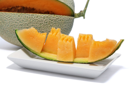 Close-up of sliced orange melon in pieces on a white plate, white background.