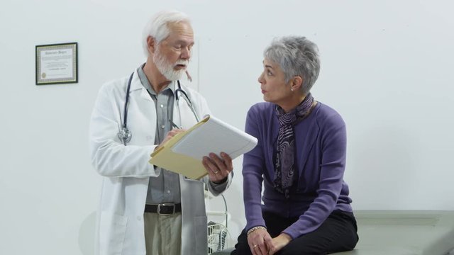Elderly doctor taking notes and talking to patient