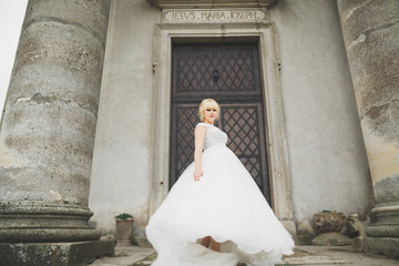 Naklejka premium Beautiful elegant bride with perfect wedding dress and bouquet posing near old castle
