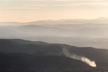 Valley filled by mist, with smoke in the foreground and distant mountains and hills in the background