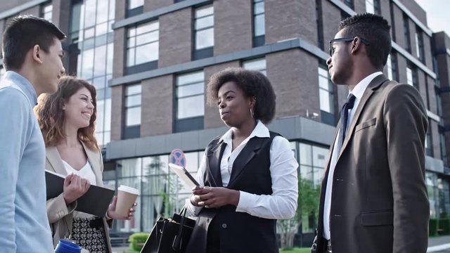 Slowmo of diverse business team standing together outdoors at sunny day, listening to African businesswoman and smiling