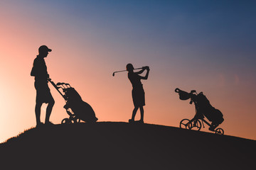 Fototapeta na wymiar silhouettes of man with his son golfers playing golf on golf course at sunset
