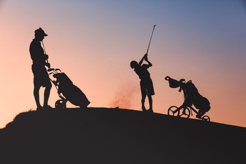 Fototapeta na wymiar silhouettes of man with his son golfers playing golf on golf course at sunset
