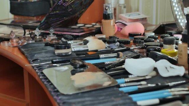 The make-up worker's desk. Many cosmetics are scattered on the table. The make-up artist paints the model.