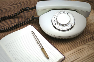 Old telephone, open phone book with blank pages with copy space and pen on wooden table surface. Contact us.