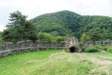 Fototapeta premium Old ruined stone wall of ancient Cisnadioara fortress in Sibiu, Romania. Green grass all around. Mountains in background.