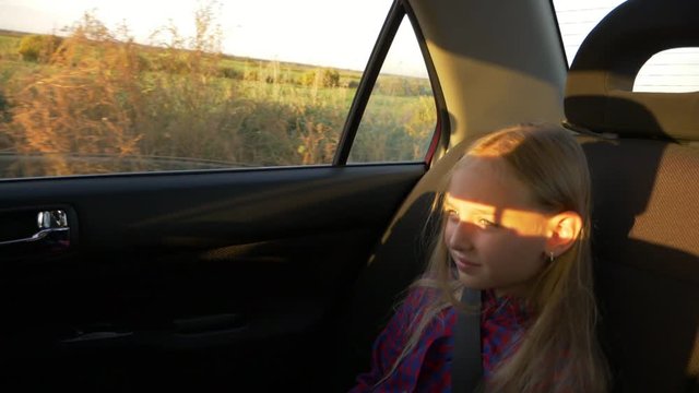 Sad serious young girl traveling by car summer evening. Rural scene at window. Girl close up handheld shot.