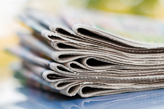 Time to read concept. Newspapers folded and stacked on the blue surface and blur background. Closeup, selective focus