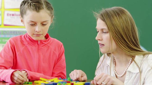 Teacher helping young girl with building blocks