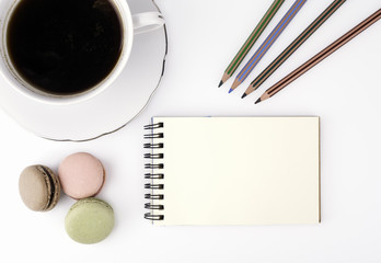 Free space for text, marketing and business information. Cake macaron and cap of coffee, notebook and colored pencils on a white background